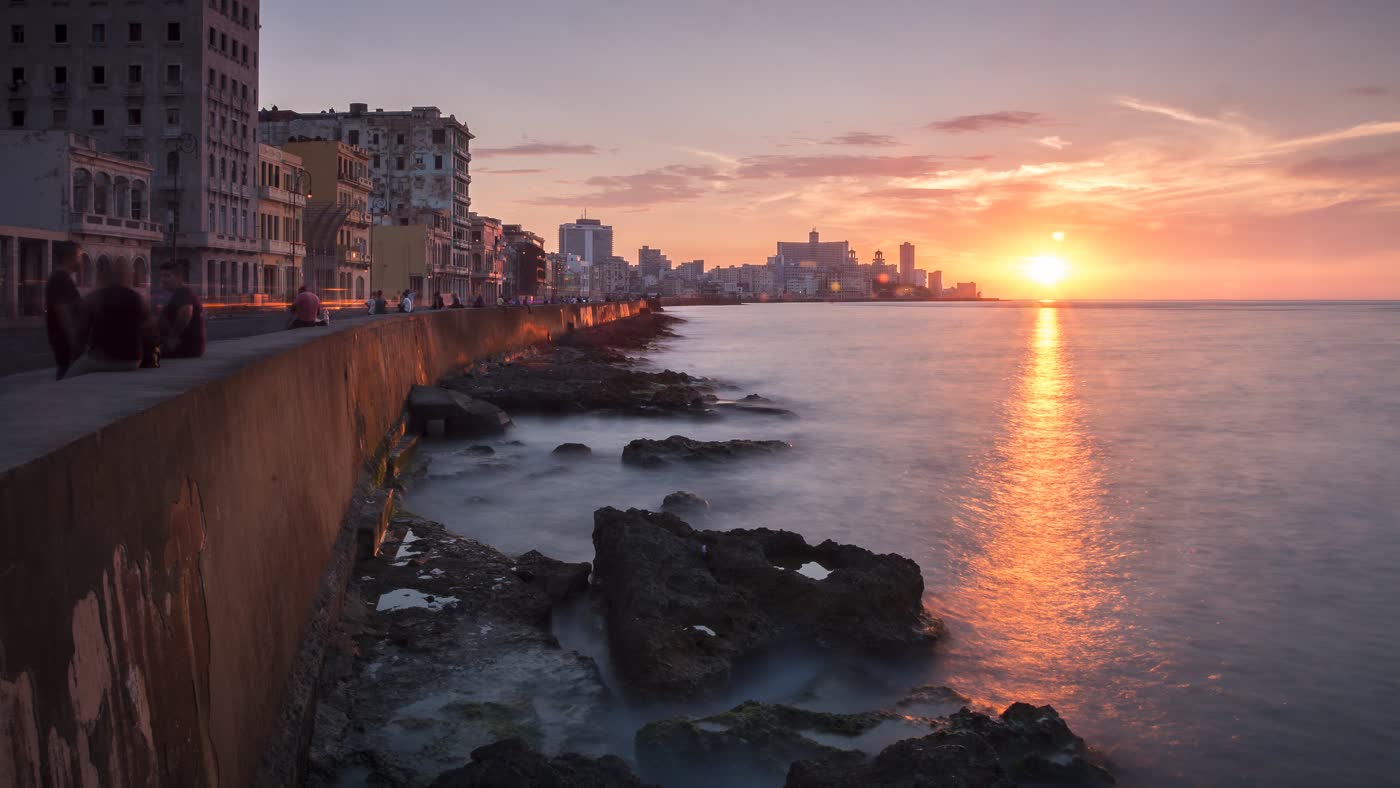 The Havana Malecón at sunset, with the sun over the sea and the city's buildings in the background