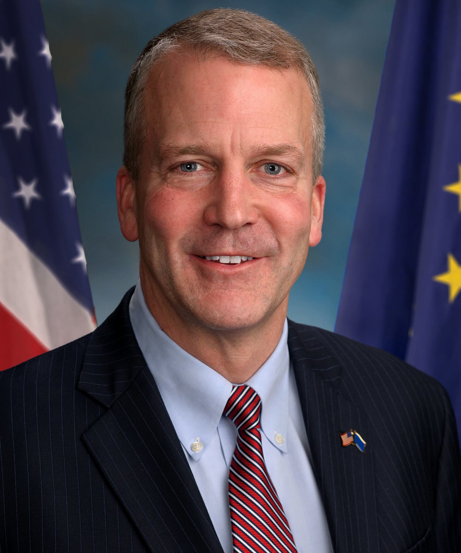 Retrato oficial del senador Dan Sullivan, de Alaska, con traje y corbata delante de una bandera