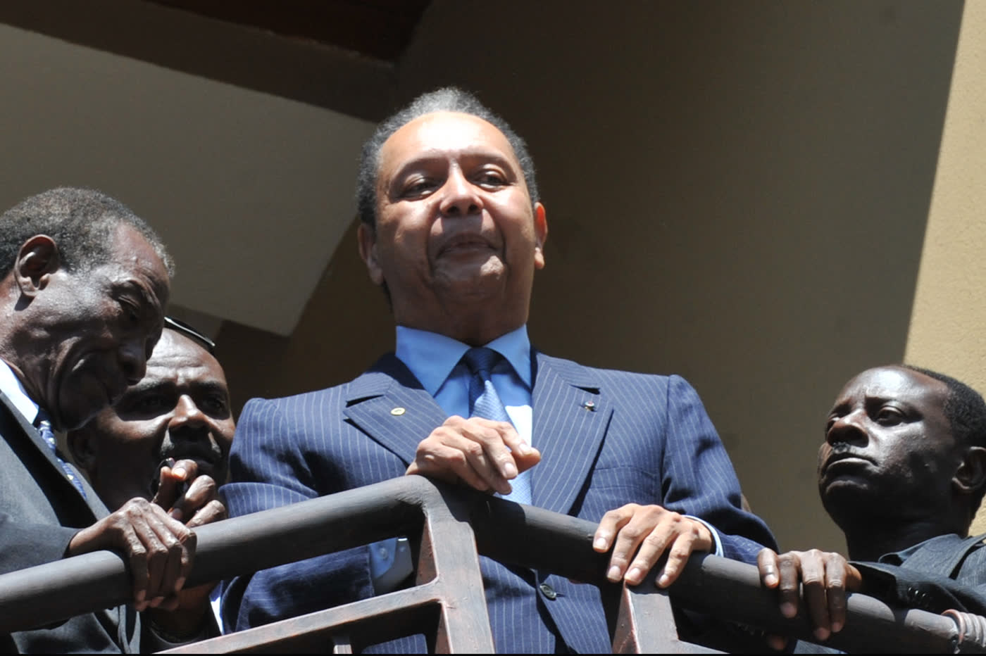 Jean-Claude Duvalier, in a blue suit, waving from a balcony surrounded by other people